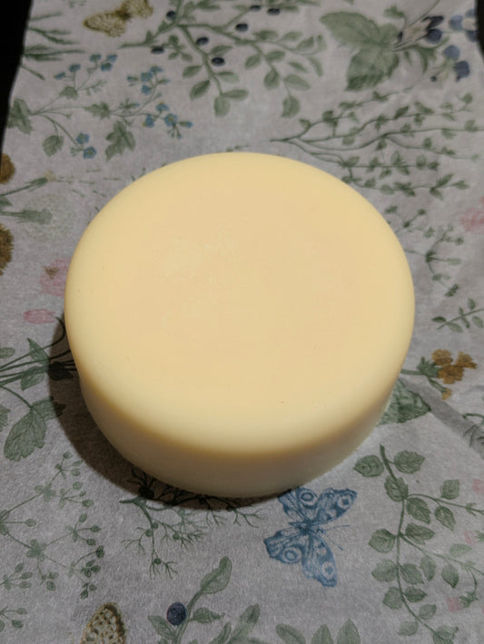 A round, pale dish soap bar, on floral-patterned tissue paper.