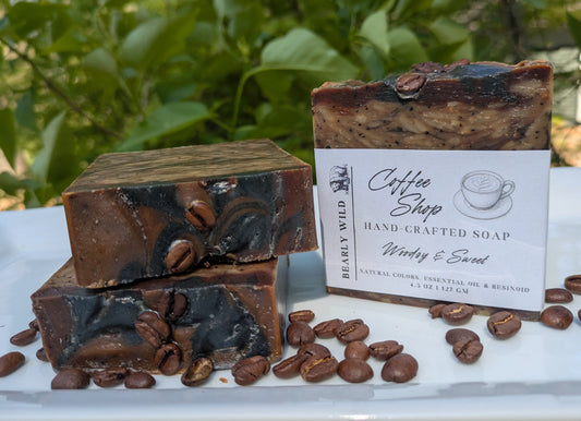 Three handcrafted soaps with coffee beans and one labeled "Coffee Shop" on a white surface with greenery in the background