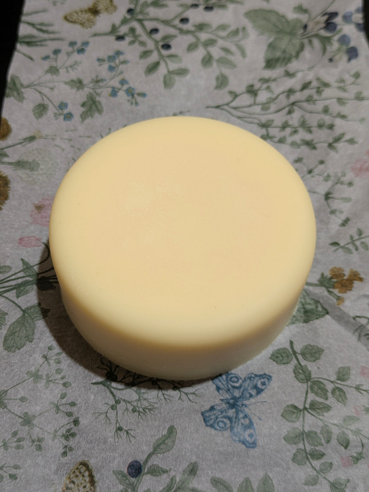 A round, pale dish soap bar, on floral-patterned tissue paper. 